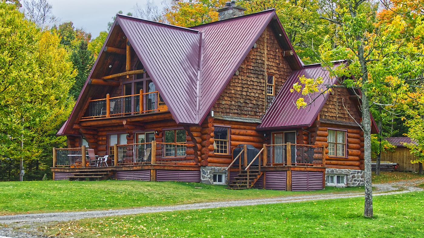 Timber-clad New England home with a new metal gable roof, set in fall foliage